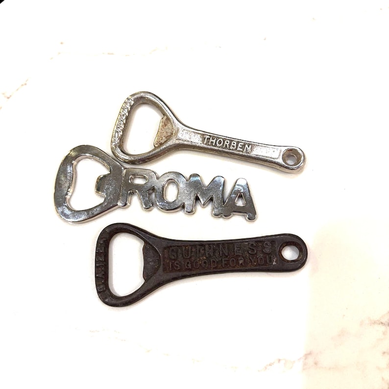May include: Three metal bottle openers. The top one is silver and reads "THORBEN". The middle one is silver and reads "ROMA". The bottom one is dark brown and reads "GUINNESS IS GOOD FOR YOU".