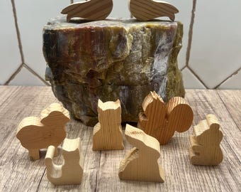 May include: Wooden bird ornaments perched on a textured rock formation, with a collection of small wooden animal figurines below. The figurines include a sheep, cat, fox, squirrel, rabbit, and bear. The wood has a natural grain.