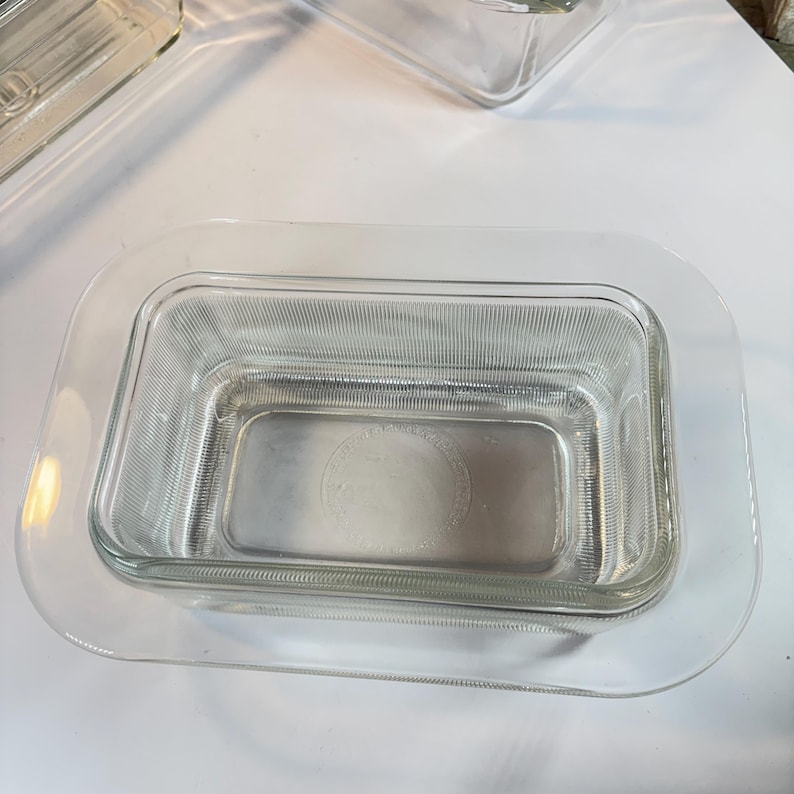 May include: Clear glass rectangular baking dish with a ribbed pattern. The dish sits inside a larger clear glass tray. The design is simple and functional, suitable for baking and serving.