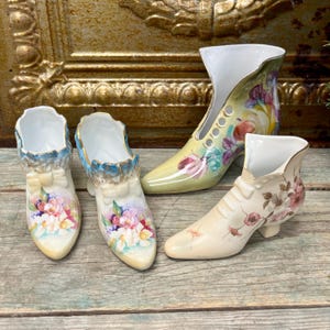 May include: Set of four porcelain shoe-shaped vases with floral designs. The vases are in various shades of white, yellow, and pink.