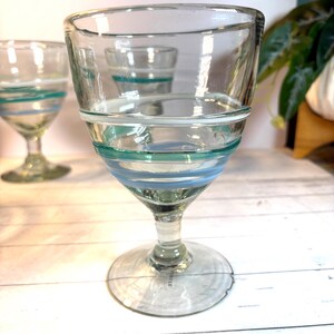 May include: Clear glass goblets with teal and light blue stripes. The stemware has a wide bowl and a round base. The design features a series of horizontal stripes around the bowl, adding a decorative touch to the glassware.