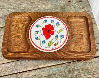 May include: A wooden serving tray with a ceramic tile inset featuring a red flower with blue and green floral accents. The tile is surrounded by a wooden frame with two smaller serving areas.