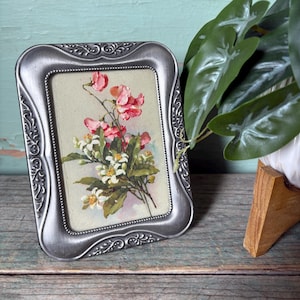 Cartão postal vintage emoldurado, moldura prateada com detalhes em estilo Art Nouveau, ilustração de buquê de flores rosa e branco dos anos 30-40.