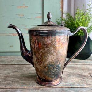 May include: A silver teapot with a tarnished finish. The teapot has a rounded body and a spout with a curved handle.