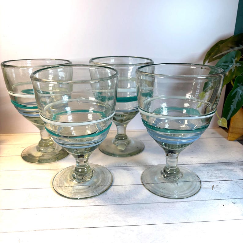 May include: Four clear glass goblets with a decorative design. Each goblet features a series of horizontal stripes in shades of blue and white around the bowl. The goblets have a classic stem and base.