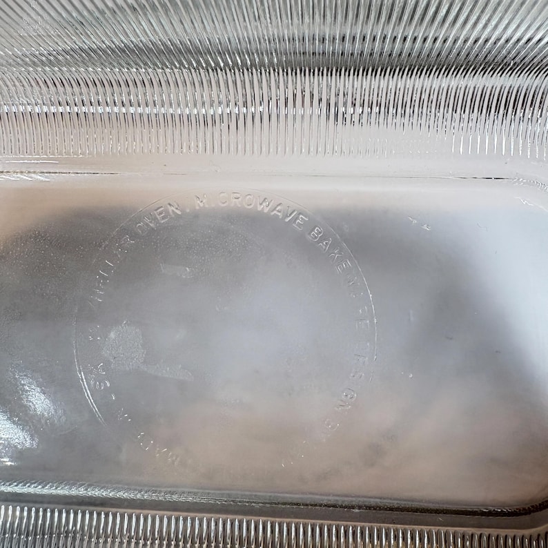 May include: Clear glass rectangular baking dish with a ribbed design on the sides. The text "Microwave Bake" is visible in a circular pattern. The dish is designed for oven and microwave use.