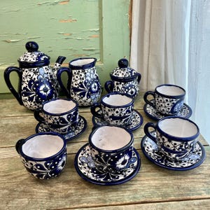 Könnte beinhalten: Ein blaues und weißes Keramik-Tee-Set mit einer Teekanne, einer Kanne, einem Zuckertopf und vier Tassen und Untertassen. Das Set hat ein Blumenmuster mit blauen Blumen und weißen Akzenten.