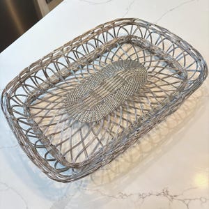 Puede incluir: Juego de dos cestas de alambre plateado. La cesta más grande es rectangular con esquinas redondeadas y un diseño tejido. La cesta más pequeña, de forma ovalada, se encuentra dentro de la más grande. Las cestas están vacías.