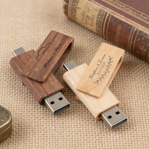 Könnte beinhalten: Zwei USB-Sticks aus Holz. Einer ist dunkelbraun mit dem Text "Michael + Phete" und einer Kamera-Grafik. Der andere ist helles Holz mit dem Text "Kristine & Kevin 20.01.2026" und einem floralen Design. Beide haben einen USB-Anschluss.