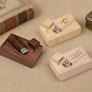 Könnte beinhalten: Drei USB-Sticks aus Holz mit passenden Boxen. Einer ist dunkelbraun, einer hellbraun und einer hat eine natürliche Holzfarbe. Jeder hat einen USB-Anschluss und einen Deckel. Der dunkelbraune Stick trägt den Text "Happy Life".