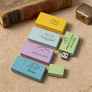 May include: A collection of colorful USB flash drives in yellow, blue, purple, and green. Each drive has a unique design and text, including names and dates. The drives are arranged on a textured surface.