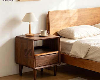 Pode incluir: Uma mesa de cabeceira de madeira castanha escura com uma gaveta e uma prateleira aberta. Uma pequena lâmpada com uma sombra bege e uma chávena e pires estão em cima. A mesa de cabeceira está ao lado de uma estrutura de cama de madeira. A marca "METALSTORMTH" é visível.