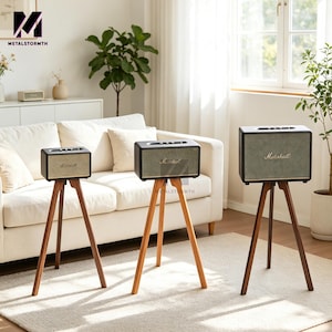 Può includere: Tre altoparlanti Marshall su supporti a treppiede in legno. Gli altoparlanti hanno una forma rettangolare con un fronte beige chiaro e finiture nere. Il logo Marshall è visibile sulla parte anteriore. I supporti sono in legno con tre gambe.