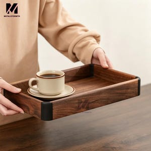 May include: A rectangular wooden serving tray with a coffee cup and saucer. The tray is dark brown with black corner accents. The cup and saucer are cream-colored with a brown trim. The tray is being held by a person.