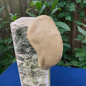 May include: A gold glitter fabric hat shaped like a teardrop. The hat is sitting on a stone pedestal.