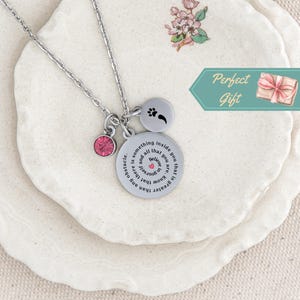May include: A silver necklace with a round pendant that reads "It is greater than any obstacle. Believe that you are something inside you that is and all that you know." The pendant has a small pink crystal and a paw print charm.