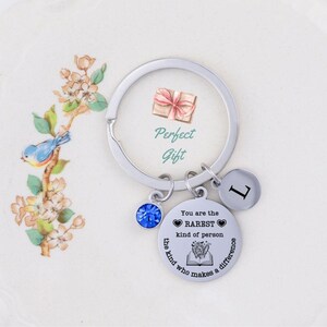 May include: Silver keychain with a blue crystal charm, a silver charm with the text "You are the RAREST kind of person the kind who makes a difference" and a silver charm with the letter "L".