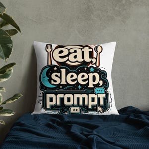 May include: A square throw pillow featuring a white background with a graphic design that includes a fork, spoon, a crescent moon, and the text "eat, sleep, prompt" in a stylized font. The design incorporates dark blue and beige color accents.
