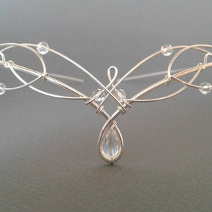 Puede incluir: Diadema de alambre plateado con un cristal en forma de lágrima y cristales más pequeños a lo largo del alambre.
