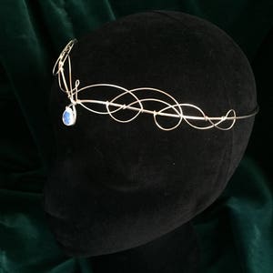 Op de afbeelding: Zilveren draadkroon met een blauwe edelsteenhanger. De kroon bevindt zich op een zwart mannequinhoofd.