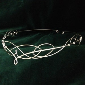 Peut inclure: Une couronne en fil d'argent avec un motif de nœud celtique. La couronne est faite de fil fin et a un design délicat et complexe.