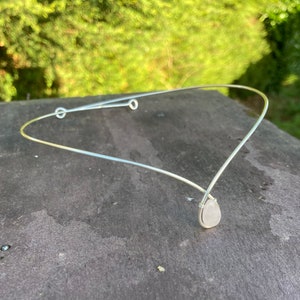 Pode incluir: Uma faixa de cabelo de fio de prata com um pingente de pedra branca em forma de lágrima.