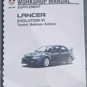 Op de afbeelding: Een werkplaats handboek supplement voor de Mitsubishi Lancer Evolution VI Tommi Makinen Edition. De omslag toont een zwart-wit foto van de auto met de tekst "LANCER" aan de zijkant.