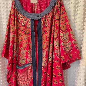 May include: A red and gold patterned kimono with a denim trim and a single button closure. The kimono has a large pocket on the left side.