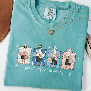 Può includere: T-shirt turchese Comfort Colors con grafica di quattro oche in abiti da ufficio. Le parole "front office secretary" sono stampate sotto. Una collana d'oro con un ciondolo è appoggiata sulla maglietta. Taglia S.