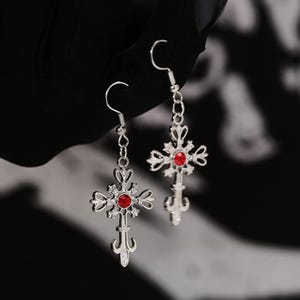 Puede incluir: Un par de pendientes de plata con colgantes de cruz de piedra roja.