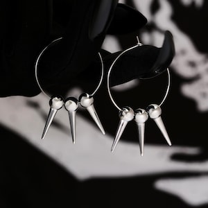 May include: A pair of silver hoop earrings with three spikes on each hoop. The spikes are rounded at the top and pointed at the bottom.
