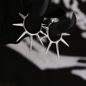 May include: A pair of silver hoop earrings with a starburst design. The earrings have sharp points and are a bold statement piece.