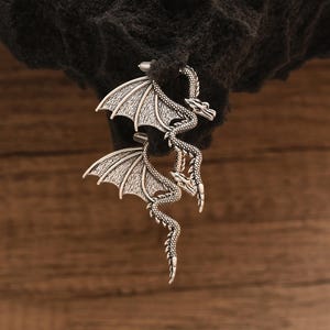 May include: Silver dragon earrings with intricate details. The dragon is depicted with wings spread and a long tail.