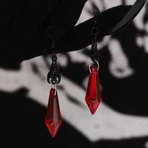 May include: A pair of dangle earrings with black metal chains and red teardrop-shaped crystal accents.