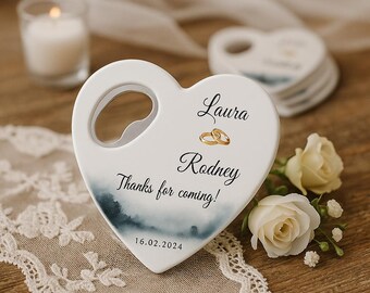 May include: A white heart-shaped bottle opener with a silver opener. The opener has the names "Laura" and "Rodney" with gold rings, and the text "Thanks for coming!" and the date 16.02.2024. The opener has a watercolor design.