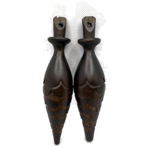 May include: Two dark brown wooden finials with a carved, scaly design. The finials are shaped like a cone and have a small hole at the top.