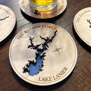May include: Wooden coasters with a laser-cut map of Lake Lanier, with the words "The Raymer Family" and "Lake Lanier" engraved. A glass of beer sits on a coaster with "Lake Cumberland" printed on it.