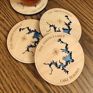 Puede incluir: Cuatro posavasos de madera con un contorno de lago azul y un dise&ntilde;o de br&uacute;jula. Los posavasos est&aacute;n personalizados con "The Smith Family" y "Lake Texoma".