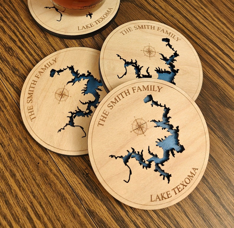 Puede incluir: Cuatro posavasos de madera con un contorno de lago azul y un dise&ntilde;o de br&uacute;jula. Los posavasos est&aacute;n personalizados con "The Smith Family" y "Lake Texoma".