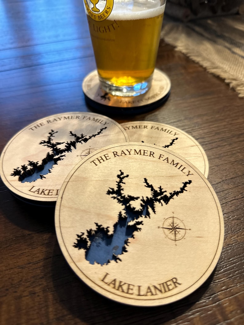 Puede incluir: Cuatro posavasos de madera con un dise&ntilde;o de Lake Lanier cortado con l&aacute;ser. Los posavasos est&aacute;n personalizados con "The Raymer Family" y presentan un dise&ntilde;o de br&uacute;jula.