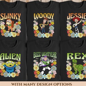 May include: Six black long-sleeved shirts featuring different Toy Story characters printed on them. Each character is surrounded by a colourful floral wreath. The characters are Slinky Dog, Woody, Jessie, Alien, Buzz Lightyear, and Rex.