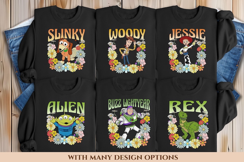 May include: Six black long-sleeved shirts featuring different Toy Story characters printed on them. Each character is surrounded by a colourful floral wreath. The characters are Slinky Dog, Woody, Jessie, Alien, Buzz Lightyear, and Rex.