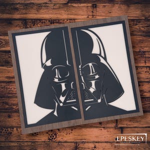 Può includere: Un'opera d'arte incorniciata in legno con una silhouette in bianco e nero del casco di Darth Vader. L'opera d'arte è divisa in due pannelli, ogni pannello mostra un lato diverso del casco.