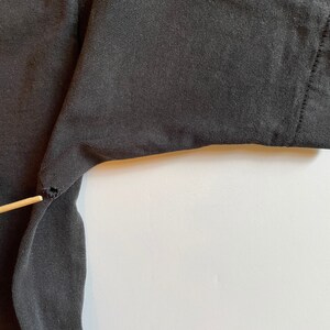 K&ouml;nnte beinhalten: Nahaufnahme eines schwarzen T-Shirts mit einem kleinen Riss in der N&auml;he der &Auml;rmelnaht.