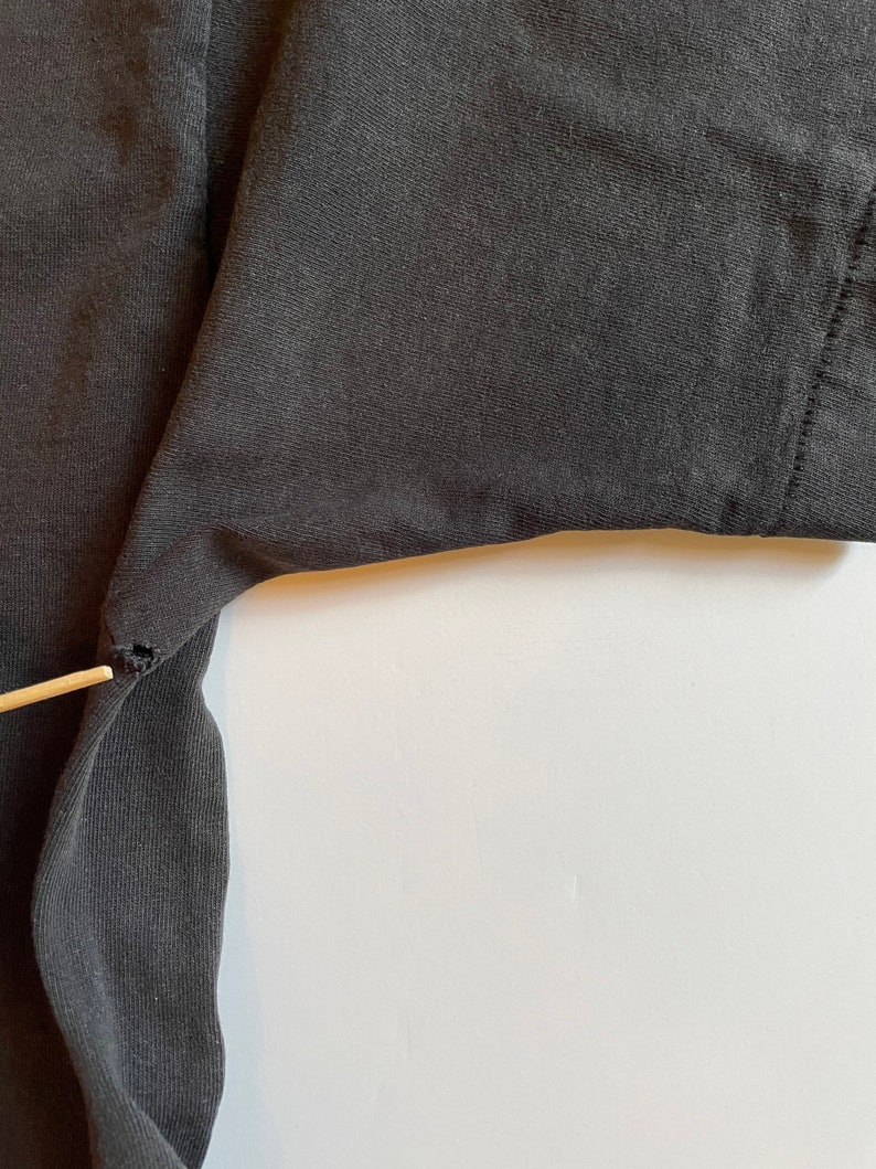 K&ouml;nnte beinhalten: Nahaufnahme eines schwarzen T-Shirts mit einem kleinen Riss in der N&auml;he der &Auml;rmelnaht.