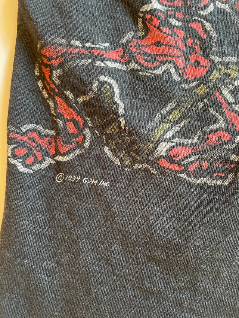 K&ouml;nnte beinhalten: Schwarzes T-Shirt mit einem roten und wei&szlig;en grafischen Aufdruck eines Schmetterlings. Das Shirt hat den Text "&copy; 1999 GDM INC" unten aufgedruckt.