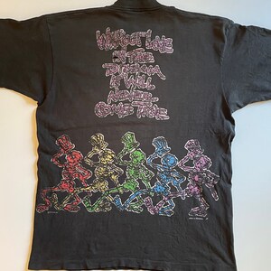 K&ouml;nnte beinhalten: Schwarzes T-Shirt mit einem Aufdruck von tanzenden Skeletten, die Zylinder tragen. Der Text "Without Love in the Dream It Will Never Come True" ist auf dem Shirt aufgedruckt.