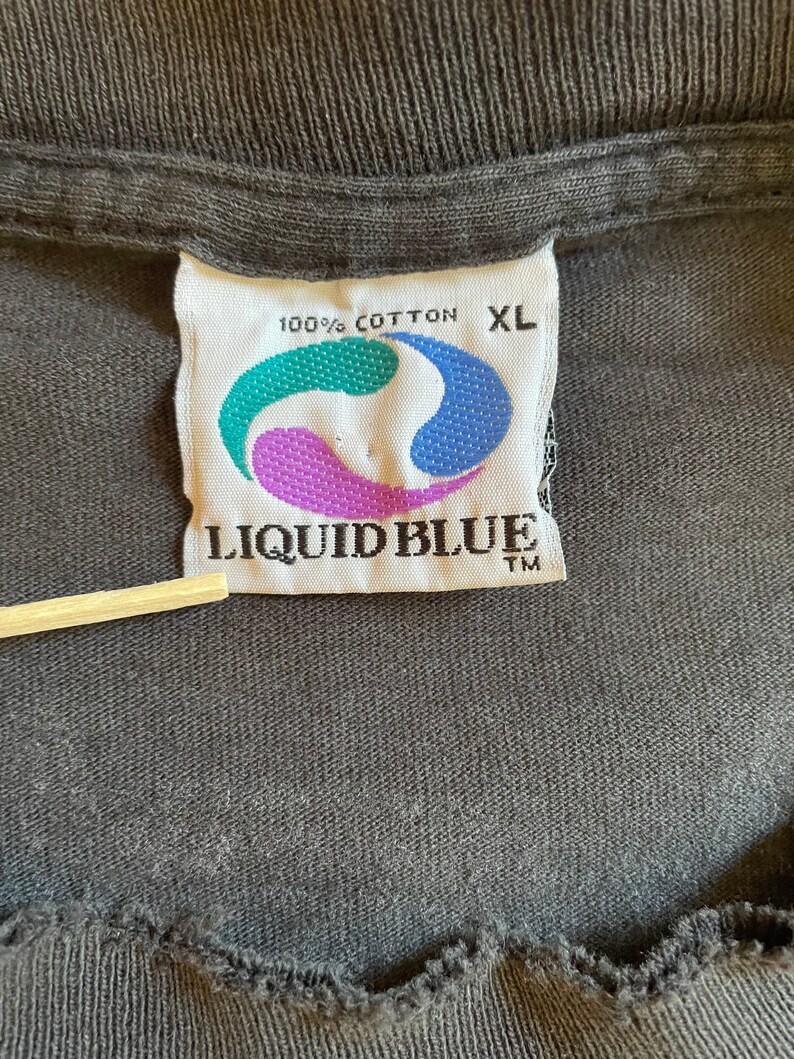 K&ouml;nnte beinhalten: Ein wei&szlig;es Etikett mit blauen und gr&uuml;nen Akzenten, auf dem "100% Baumwolle XL LIQUID BLUE TM" steht.