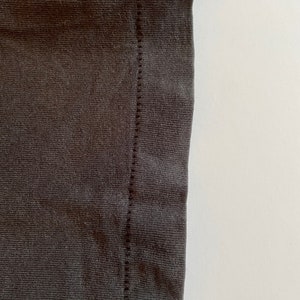 K&ouml;nnte beinhalten: Nahaufnahme der Naht an einem dunkelgrauen T-Shirt. Die Naht ist eine gerade Linie aus N&auml;hten.