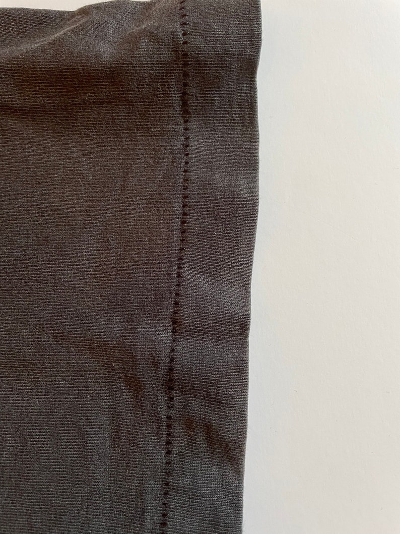 K&ouml;nnte beinhalten: Nahaufnahme der Naht an einem dunkelgrauen T-Shirt. Die Naht ist eine gerade Linie aus N&auml;hten.